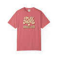 Watermelon colored Play More Adult Less pickleball t-shirt with playful cream script typography.