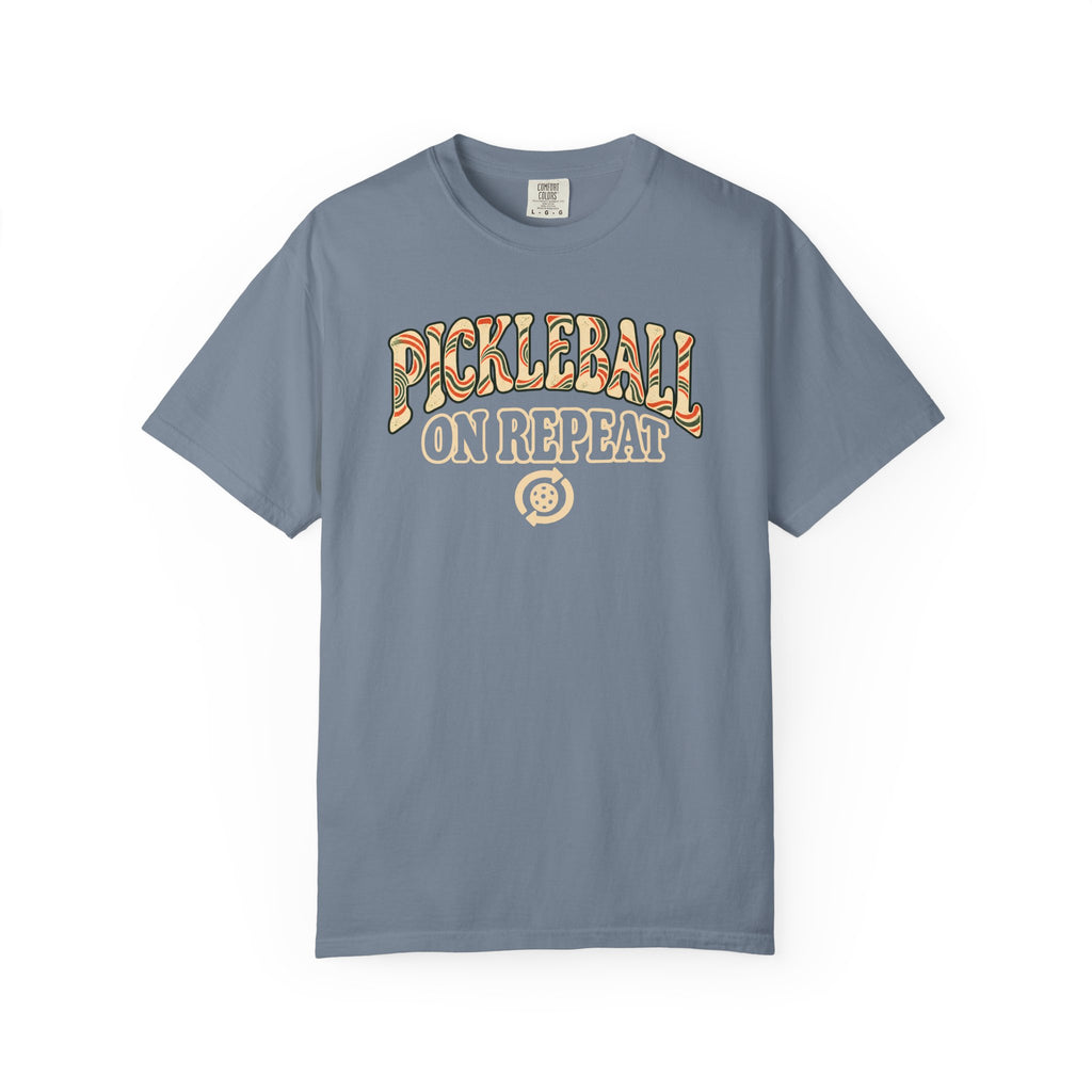Blue-gray colored Pickleball On Repeat pickleball t-shirt with warm retro varsity-style typography.